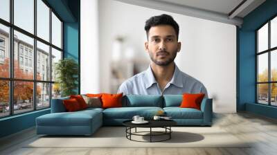 Serious Indian guy in casual blue shirt posing for camera standing alone in modern living room. Portrait of unsmiling millennial generation man, single homeowner or tenant head shot, profile picture Wall mural