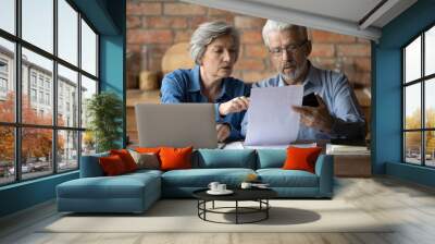 Serious mature couple checking financial documents, domestic bills, planning budget together, sitting at desk with laptop, senior man and woman counting taxes, discussing bank debt or loan payment Wall mural