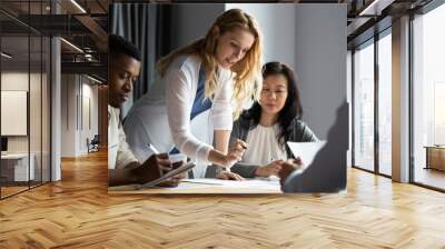 Serious millennial blonde female team leader analyzing financial or marketing paper document, reporting research results to focused multiracial young and older business partners colleagues at office. Wall mural