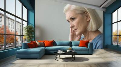 Serious thoughtful blonde elderly woman worried about health problems, thinking over retirement, touching dry facial skin, face, looking away, feeling depressed. Side casual portrait Wall mural