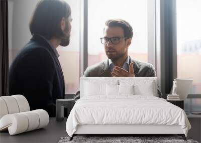 Skilled 30s businessman in eyeglasses discussing project with focused male partners at brainstorming meeting in office. Confident financial advisor or lawyer giving professional consultation to client Wall mural