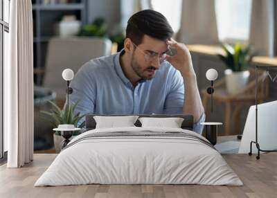 Small business owner experiences financial crisis, high costs, bank debt, money overspend concept. Man sitting at desk looks at laptop screen holding receipt feels desperate after calculating expenses Wall mural