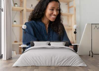 Smiling African American female employee sit at desk typing texting on modern laptop in office, happy biracial woman worker busy working on computer gadget, consult client or customer online Wall mural