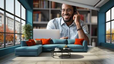 Smiling African American man in glasses and headset watch webinar on laptop making notes, happy biracial male student worker in headphones handwriting studying or working using computer Wall mural