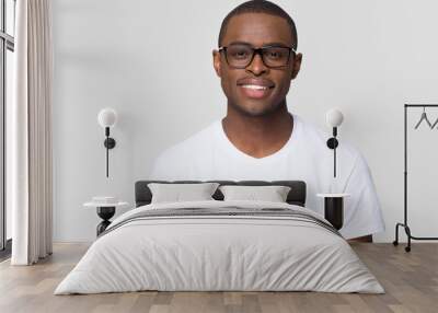 Smiling african american millennial casual man wearing white t-shirt and glasses looking at camera isolated on blank grey studio background, charming young black single male guy posing for portrait Wall mural