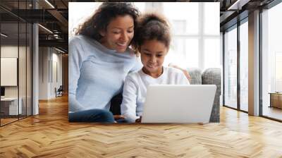 Smiling african american mother and kid daughter have fun shopping online at home, happy black mom teaching little mixed race child girl learn use laptop, watch cartoon, make video call on computer Wall mural