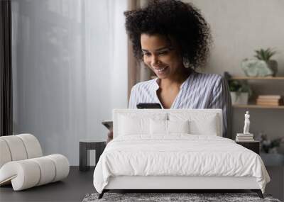 Smiling African American woman using two phones, standing at home, happy attractive young female looking at screens, browsing apps, synchronizing information on devices, setting up new smartphone Wall mural