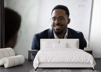 Smiling African American young businessman in glasses talk with business partner at office meeting. Happy motivated biracial man boss or CEO have talk, discuss cooperation with colleague at briefing. Wall mural