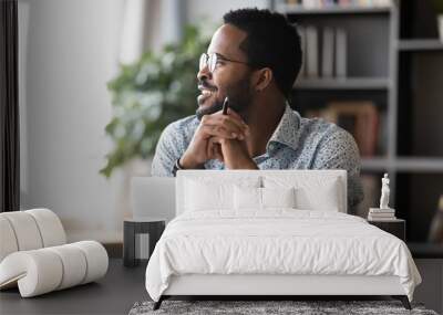 Smiling african business man look away dreaming working on laptop Wall mural