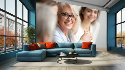 smiling aged businesswoman in glasses looking at colleague at team meeting, happy attentive female t Wall mural