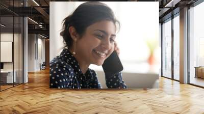 Smiling beautiful millennial indian woman talking on the phone, happy young girl caller holding cellphone laughing making call, attractive hindu female having pleasant conversation chatting by mobile Wall mural