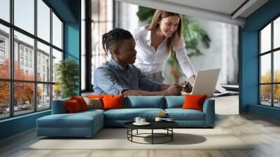 Smiling businesswoman mentor helping new African American employee with corporate software, training and teaching, standing near desk, looking at screen, supervisor checking intern work results Wall mural