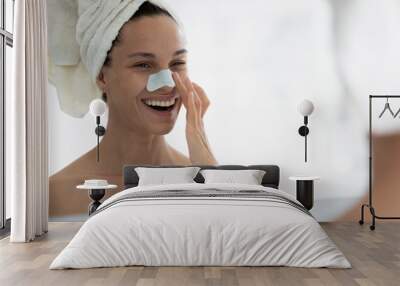 Smiling Caucasian girl after shower look in mirror apply face nose strips in bathroom, happy young woman clean cleanse pores or blackheads with beauty product for healthy skin, skincare concept Wall mural