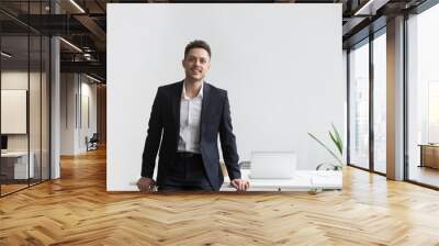 Smiling company CEO leaning back at office table posing near desk looking at camera satisfied with successful business. Concept of confidence, achievement, rewarding Wall mural