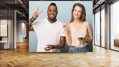 Smiling diverse man and woman with phones show peace gesture Wall mural