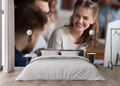 Smiling happy young woman talking with male colleagues at shared workplace, worker laughing at funny joke, reading funny news, excited business success, employees having break, pause Wall mural