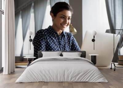 Smiling indian girl student professional typing on laptop at table Wall mural