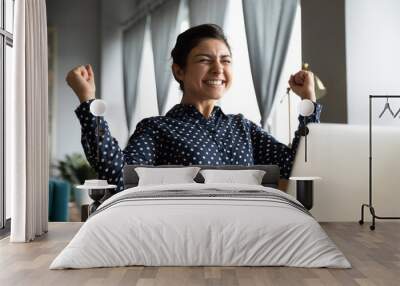 Smiling Indian woman excited by good news, work success, received great shopping or job offer, successful exam results, happy girl showing yes gesture, celebrating win, sitting at desk with laptop Wall mural