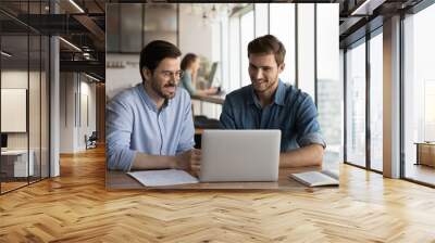 Smiling male employees colleagues work together brainstorm using modern computer gadget at meeting in office. Happy young businessmen cooperate on laptop discuss partnership. Teamwork concept. Wall mural