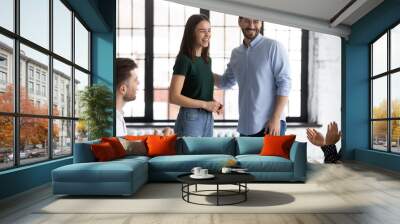 Smiling male employer introduce excited female newcomer to overjoyed diverse coworkers at office briefing, happy businessman welcome new worker at team meeting in boardroom, introduction concept Wall mural