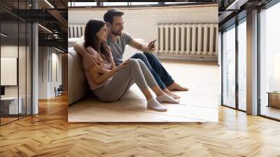 Smiling man and woman hugging, using phone, sitting on floor Wall mural