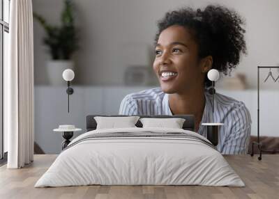 Smiling millennial African American woman relax in cozy own living room look in distance dreaming or visualizing. Happy young biracial female renter think or plan. Vision, visualization concept. Wall mural