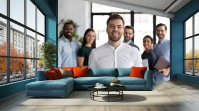 Smiling millennial student looking at camera posing for portrait in front of diverse young people group getting education at international university, happy ambitious intern receiving job at company Wall mural