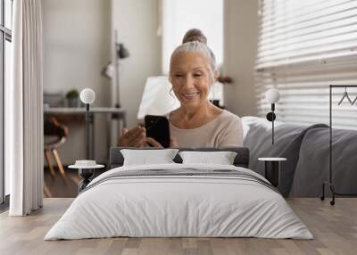 Smiling modern Caucasian senior woman look at cellphone screen have video call on gadget at home. Happy mature female use new technologies, talk on webcam virtual digital conference on smartphone. Wall mural