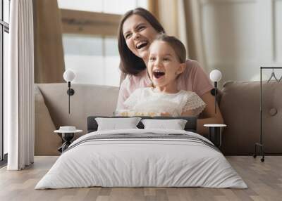 Smiling mom and little daughter watch movie eating popcorn Wall mural