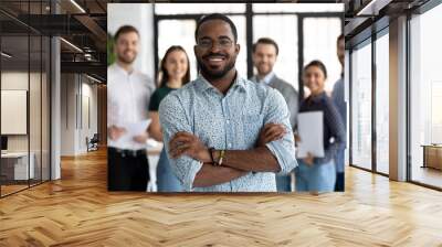 Smiling motivated African American male employee stand forefront posing together with colleagues in office, happy biracial businessman show success and leadership in business, employment concept Wall mural