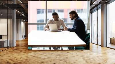 Smiling multiracial colleagues sit at office table in boardroom brainstorm using modern laptop together, multinational coworkers or partners talk discuss financial ideas work on computer at briefing Wall mural