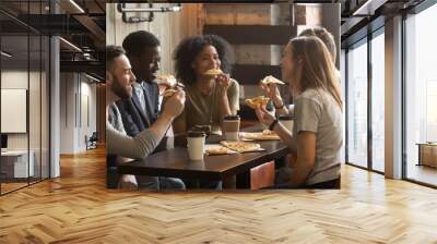 Smiling multiracial friends eating pizza and drinking coffee, laughing and having fun in restaurant, diverse millennial colleagues enjoying lunch during work break sitting at coffee table in loft cafe Wall mural