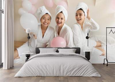 Smiling pretty young caucasian woman having fun with joyful beautiful asian girlfriends, wearing silk gowns and towels on heads, feeling relaxed after spa procedures, enjoying luxury hen party. Wall mural