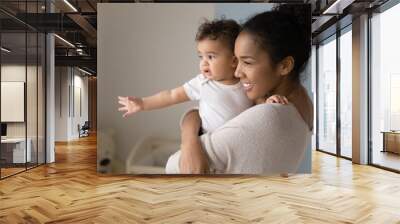 Smiling young African American mother hold in arms look in distance dream with cute little baby daughter. Happy biracial mom visualize imagine play with small toddler girl child. Parenthood concept. Wall mural