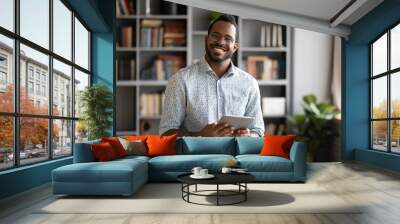 Smiling young biracial man in glasses holding digital computer tablet. Wall mural