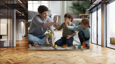 Smiling young dad give high five to excited little kids celebrate good work success playing at home together. Happy father and two small children have fun make deal engaged in funny game activity. Wall mural