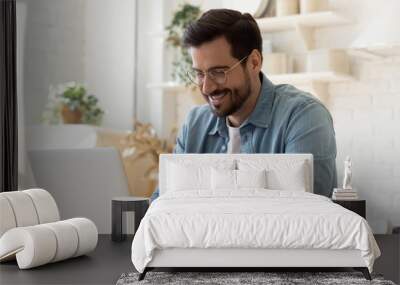 Smiling young man using laptop studying working online at home Wall mural