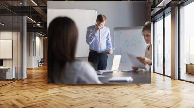 Stressed male speaker or presenter worried before making presentation for colleagues in meeting room, nervous employee wipe face scared to speak in public, afraid to present business report in office. Wall mural