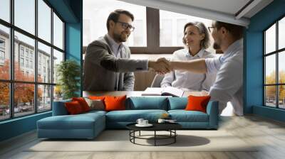 Team of business partners shaking hands after successful discussion, smiling, reaching agreement, giving greeting handshake over meeting table, working on partnership, cooperation Wall mural