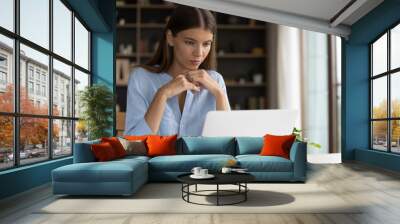 Thoughtful concentrated millennial business woman looking at computer screen, considering project problem solution, analyzing marketing data, watching educational video studying at home office. Wall mural