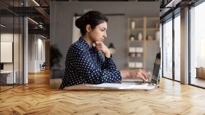 Thoughtful Indian woman looking at laptop screen, pondering task, businesswoman freelancer working on difficult project, pensive female student preparing to exam or test, doing homework Wall mural