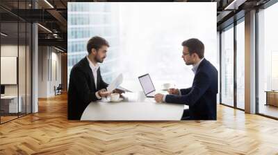 Two caucasian men sitting in front of each other at the table and discussing project results. Partners or manager and subordinate conduct performance evaluation appointment in office or meeting room Wall mural