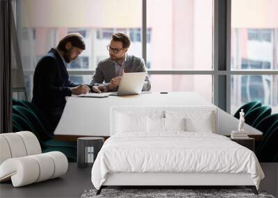 Two confident male partners signing agreement at negotiations meeting, sitting at table in boardroom. Young businessman in formal wear making deal with skilled lawyer, putting signature on contract. Wall mural