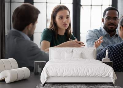 Two diverse multiethnic groups of business partners sitting at negotiation table, concentrated millennial female employee explaining plan project details to interested teammates on meeting in office Wall mural