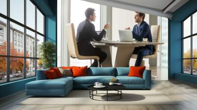 Two handsome businessmen sitting in comfortable chairs at desk with laptops in meeting room. CEO making important negotiation about companies partnership or corporate merger. Financiers planning deal Wall mural