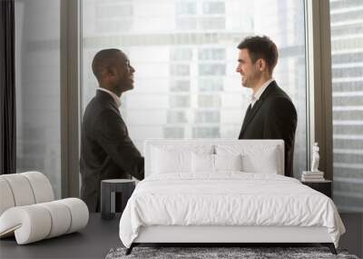 Two multinational businessmen standing together and looking in window at office. African american and caucasian business partners thinking about perspectives, dreaming of success, planning future deal Wall mural