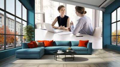 Two young pretty female colleagues talking met in modern boardroom, client and company representative negotiating in office, share information, provide assistance, sell services, engaged in teamwork Wall mural