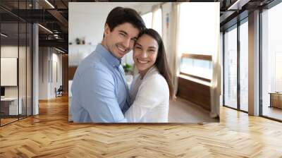 Valentines. Tender married couple newlyweds holding each other in arms looking at camera with happy smiles posing for portrait at living room of new house purchased by family credit banking programme Wall mural