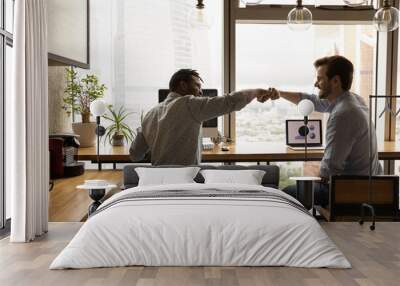 Well done, buddy. Motivated diverse young men coworkers bump fists on workplace feel excited achieve common goal. Two workers international business team members share success glad to help one another Wall mural