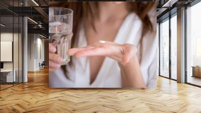 Woman holding pill and glass of water in hands taking emergency medicine, supplements or antibiotic antidepressant painkiller medication to relieve pain, meds side effects concept, close up view Wall mural